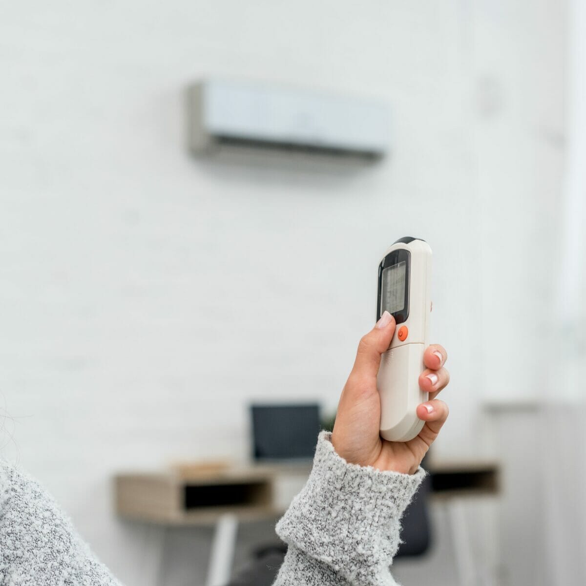 cropped shot of woman in sweater holding air conditioner remote control